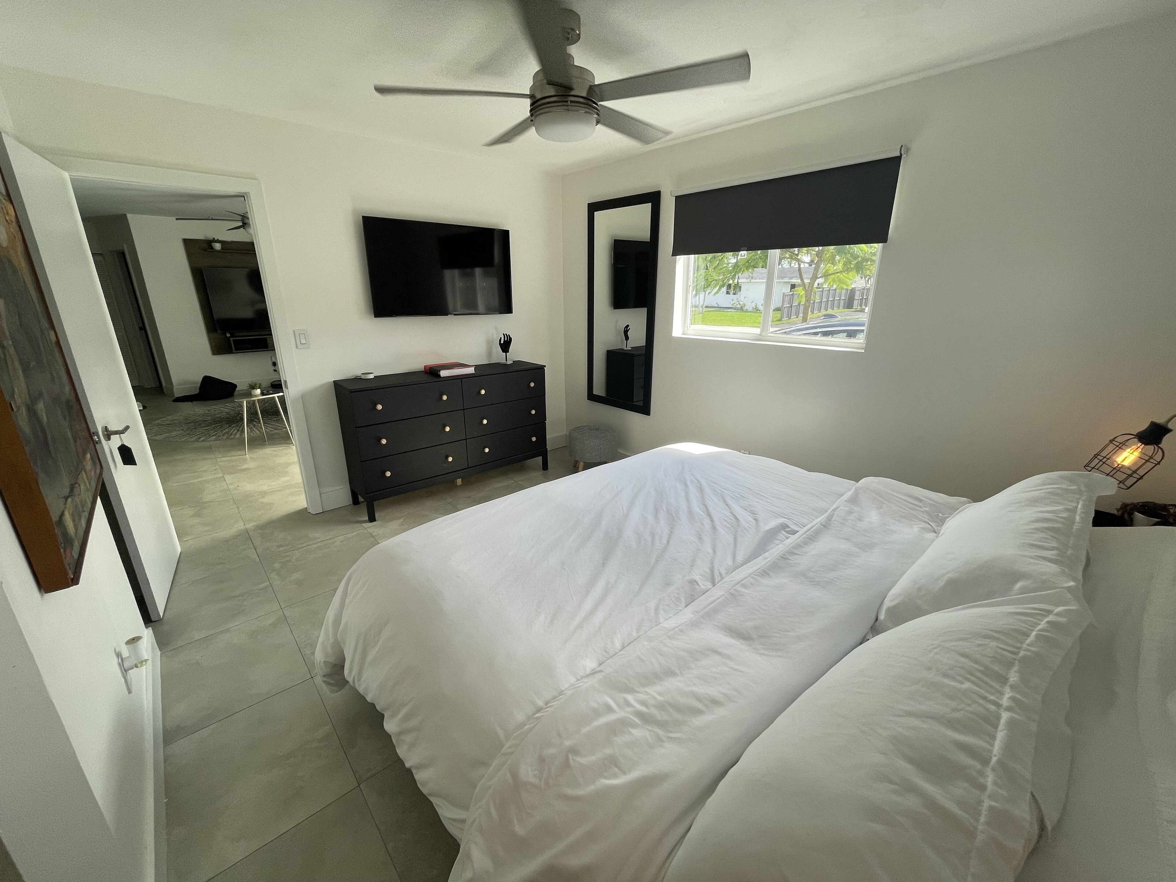 Ein Schlafzimmer mit Bett, Kommode, Fernseher und Fenster.