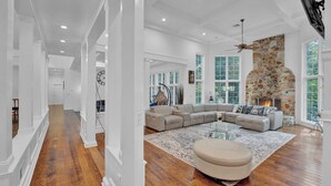 A spacious living room with a stone fireplace, large windows, and a wooden floor. - Fancy Poconos Castle & Indoor MEGA 10+ Hot Tub (East Stroudsburg)