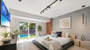 A modern bedroom with a large bed, a TV, a desk, and a view of a swimming pool. - Family getaway • Pool • BBQ • Golf • BB Court (Miami)
