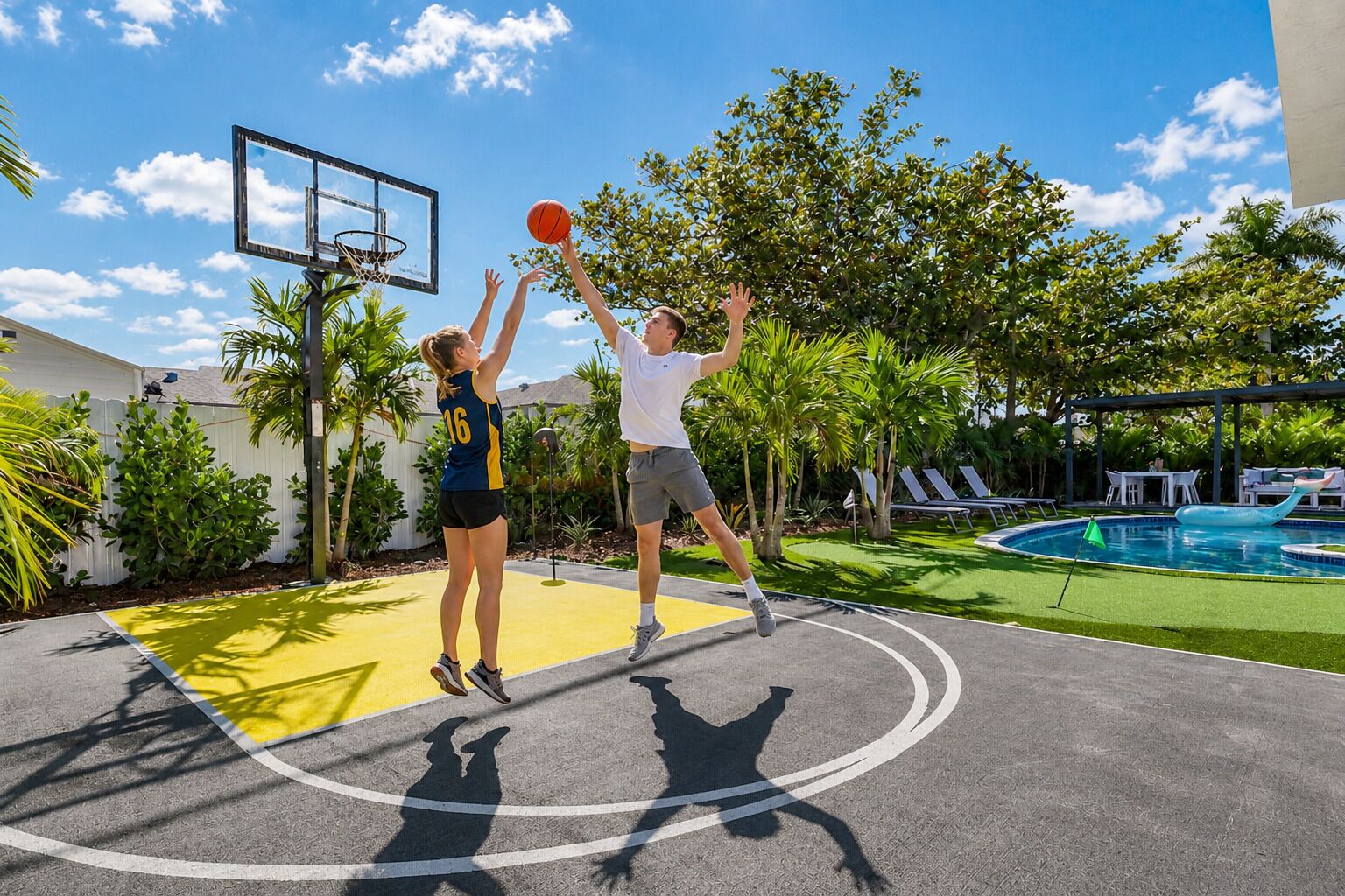 An outdoor basketball court with a pool and lounge chairs in the background.