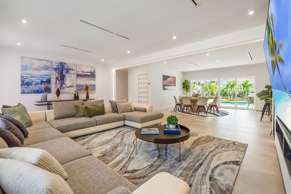 A spacious living area with a large sectional sofa, a coffee table, and a dining area with a view of the outdoors.