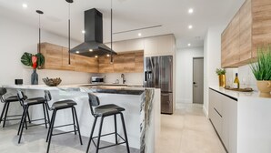 A modern kitchen with a central island, bar stools, stainless steel appliances, and wooden cabinetry. - Family getaway • Pool • BBQ • Golf • BB Court (Miami)