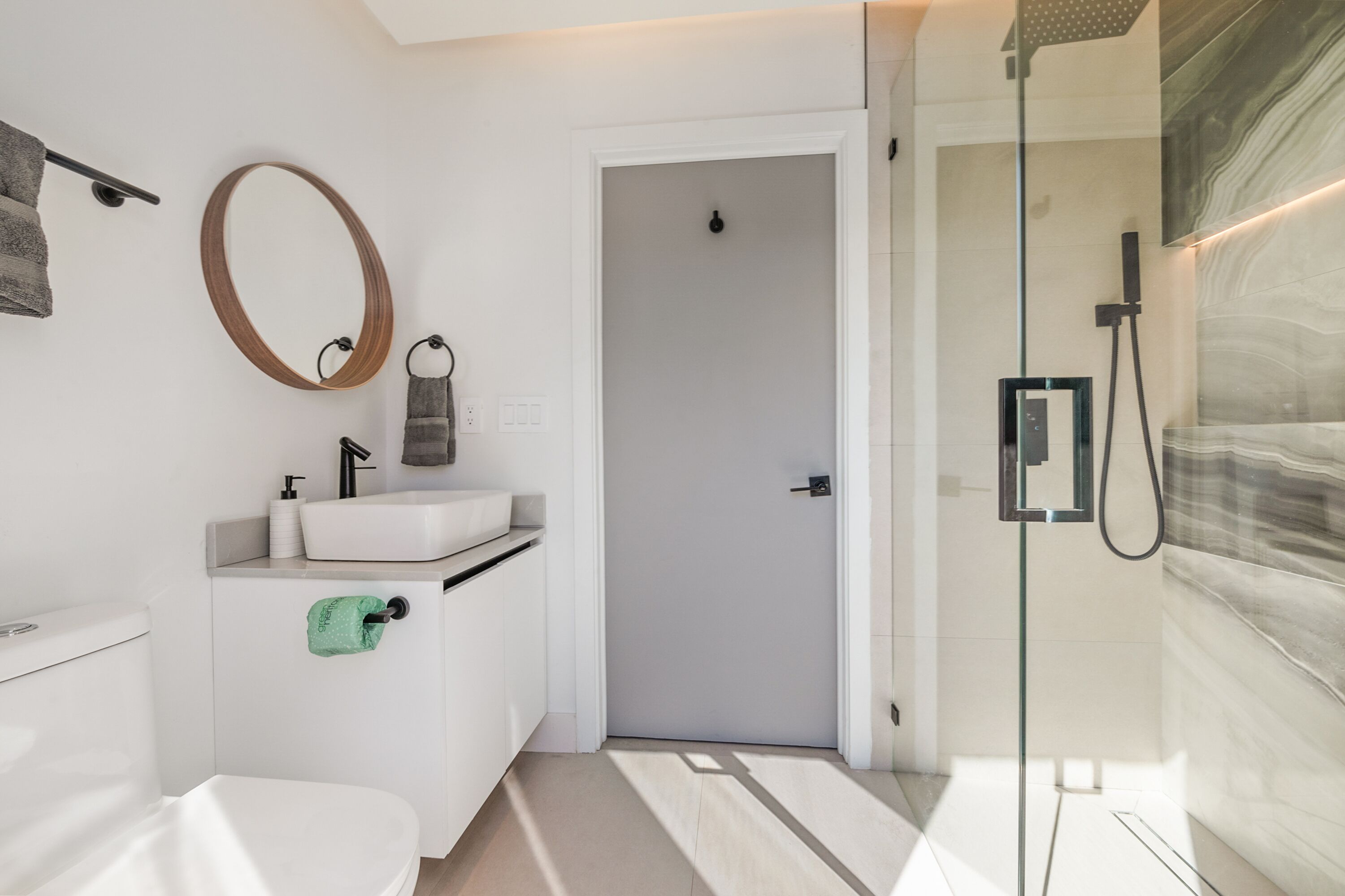 A modern bathroom with a toilet, sink, mirror, towel rack, and shower area.