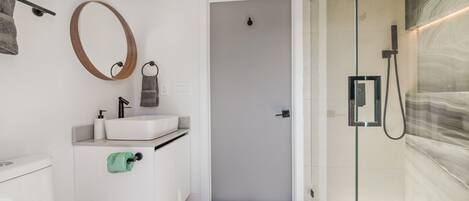 A modern bathroom with a toilet, sink, mirror, towel rack, and shower area.