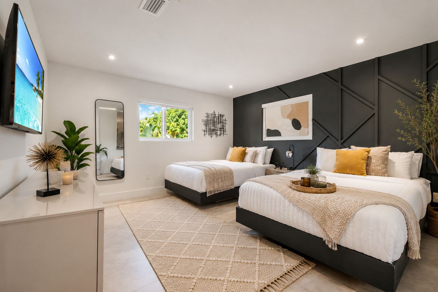 Een moderne slaapkamer met twee bedden, een televisie, een spiegel en een raam met uitzicht op groen.