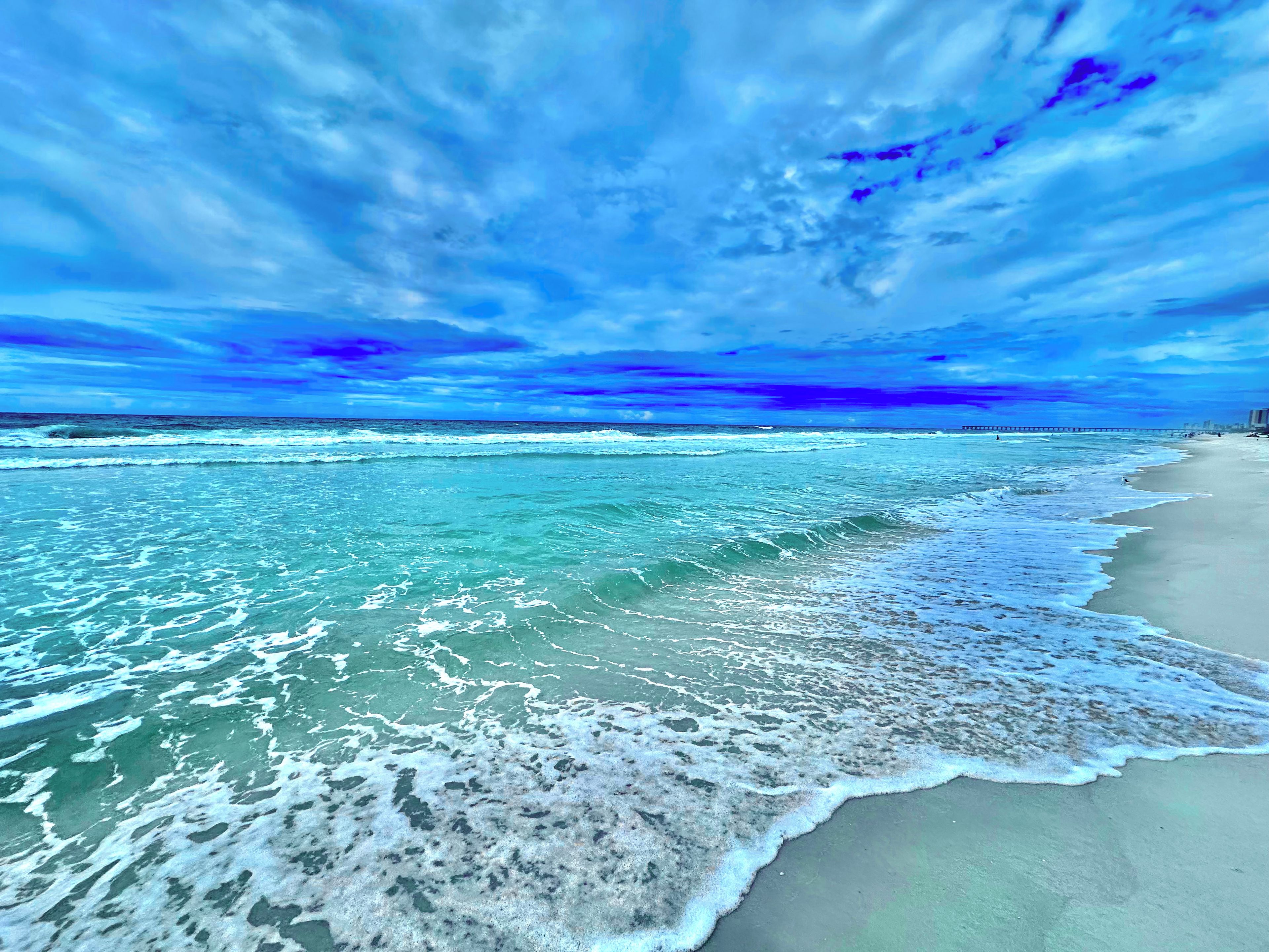 A beach with waves, a clear sky, and a distant pier.