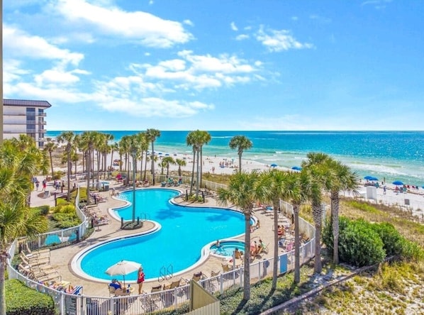 A resort with a large swimming pool, beach access, and palm trees.