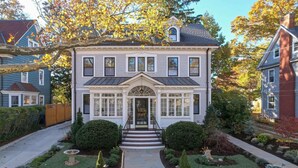 Une maison à deux étages avec un porche à l’avant, un petit jardin et une allée pavée en briques.