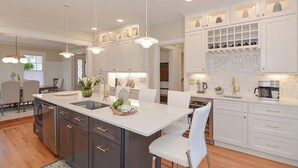 Une cuisine moderne dotée d’un îlot central, de meubles de couleur sombre, de plans de travail blancs et de luminaires suspendus.