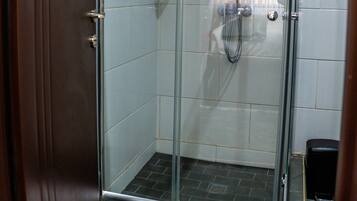 A glass-enclosed shower with a handheld showerhead and a wall-mounted faucet.