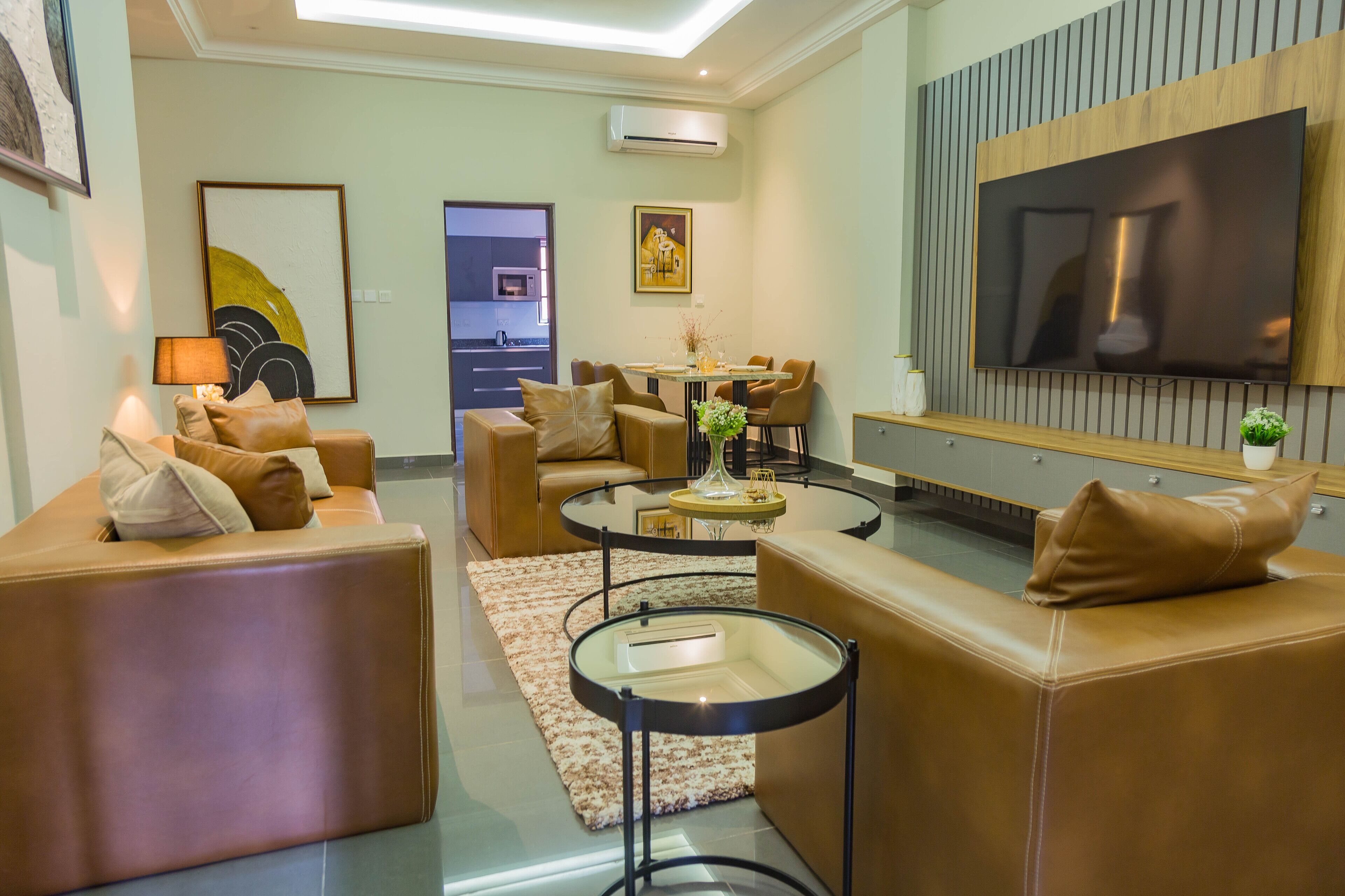 Una sala de estar moderna con sofás de cuero, una mesa de centro de vidrio y un televisor de pantalla plana montado en la pared.
