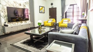 A modern living room with a flat-screen TV, a sofa, two yellow chairs, a coffee table, and a decorative vase. - Gyamfuaa Court Apartment (Kumasi)