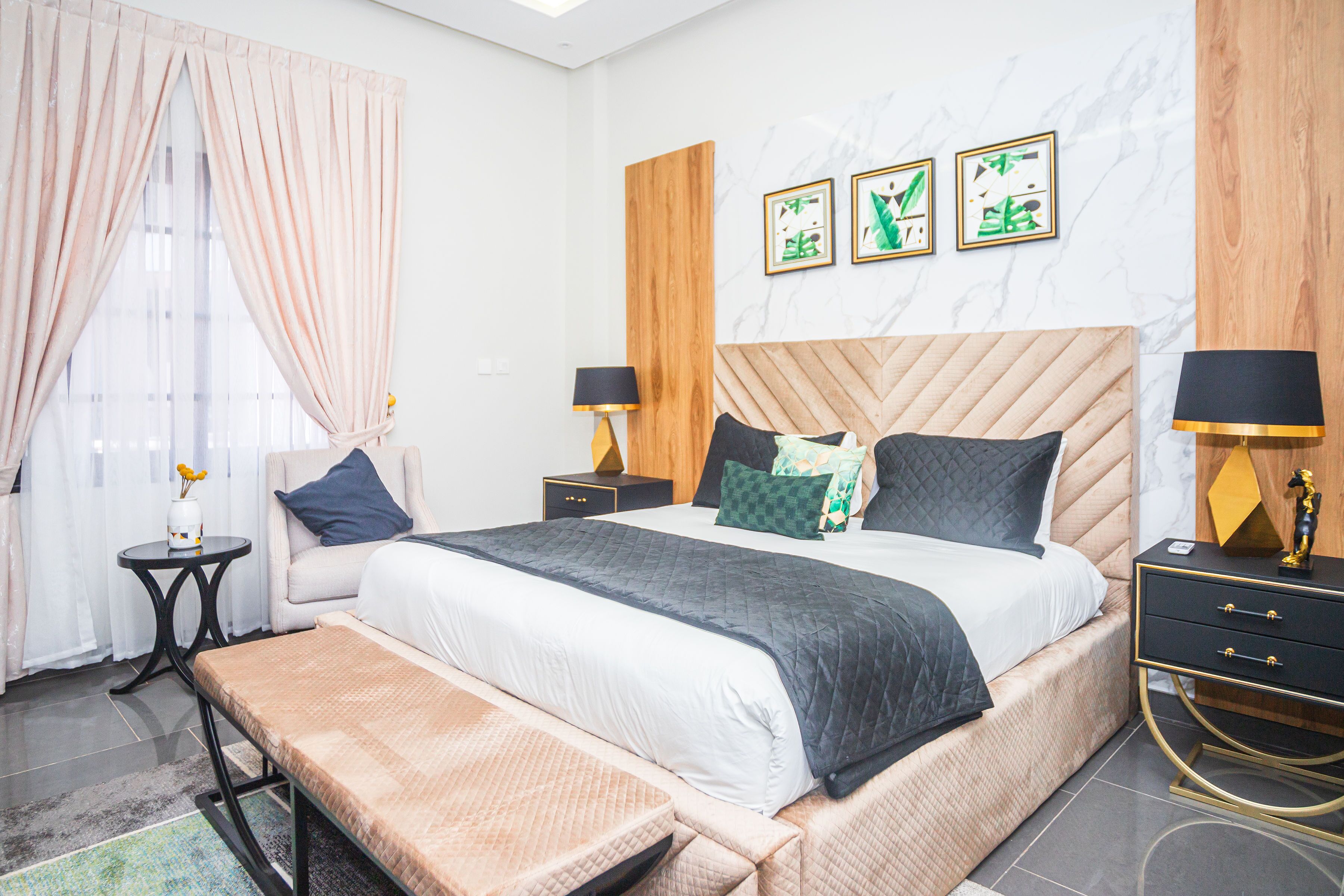 A modern bedroom with a large bed, bedside tables, a bench, and artwork on the wall.