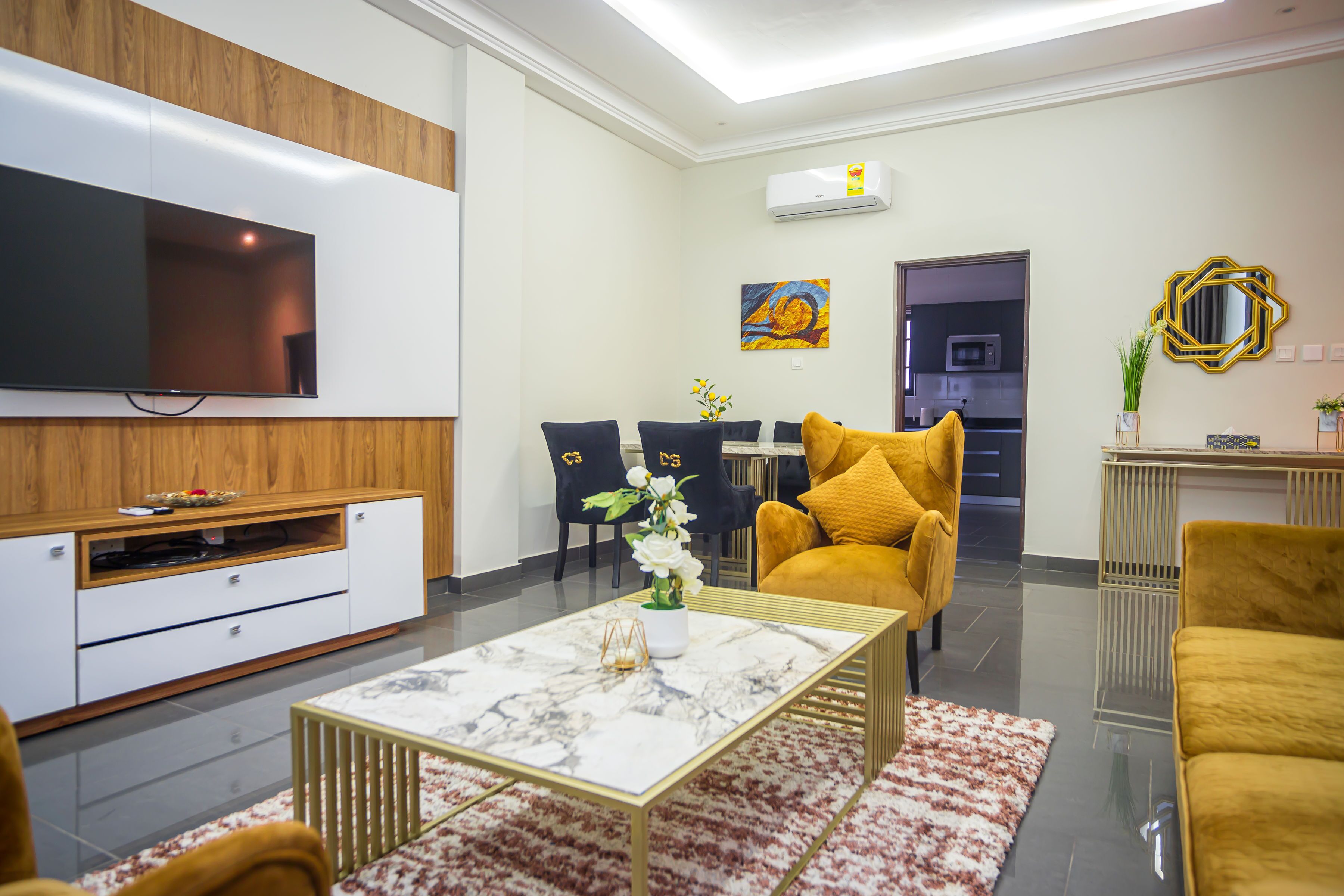 A modern living room with a flat-screen TV, a dining area with chairs, a sofa, and a coffee table.