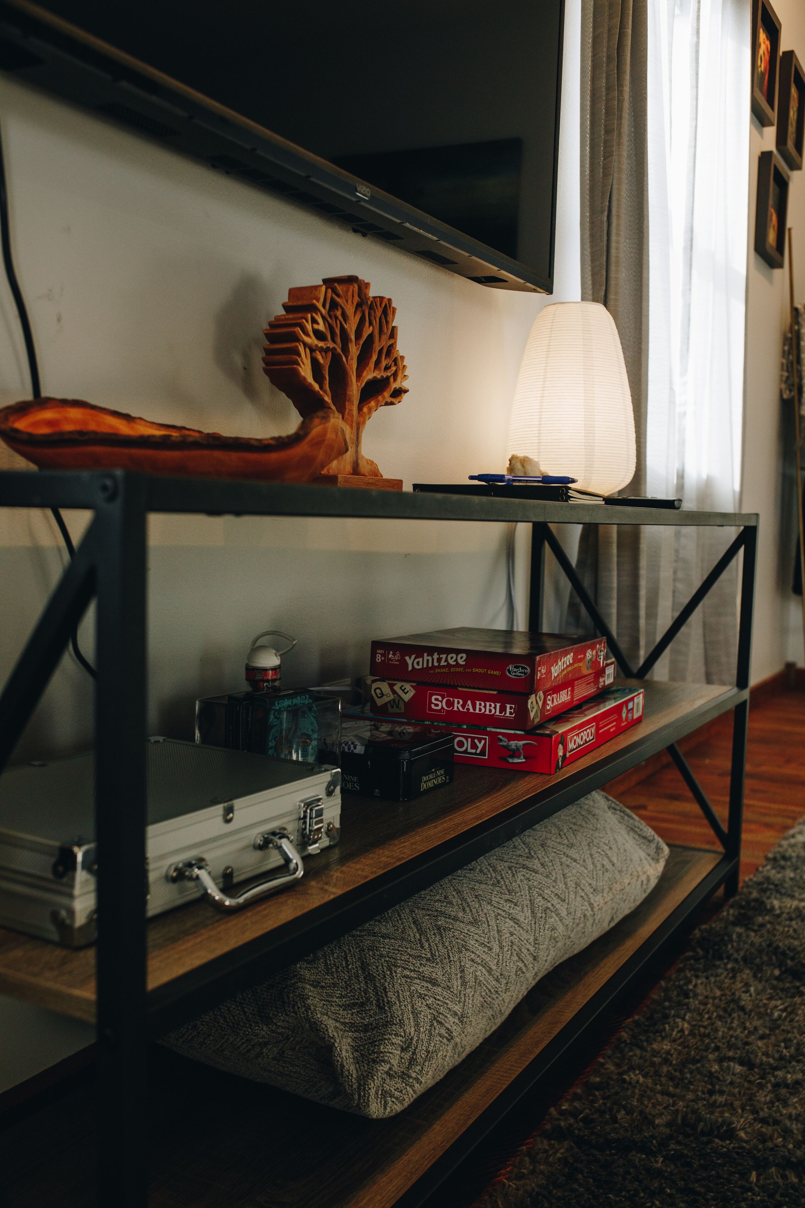 A wooden TV stand with a flat-screen TV, a decorative tree, and board games.