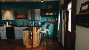 A kitchen with wooden cabinets, a central island, bar stools, and a teal wall. - Connoisseur Hideaway (Bozeman)