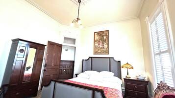A bedroom with a large bed, a dresser, a wardrobe, a chandelier, and a painting on the wall.