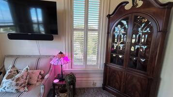A living room with a sofa, a television mounted on the wall, a cabinet with glass doors, and a window with blinds.