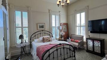 A bedroom with a bed, a TV, a chair, a table, and a dresser.