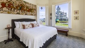 Quarto com cama grande, vista de um edifício histórico e tapeçaria na parede.