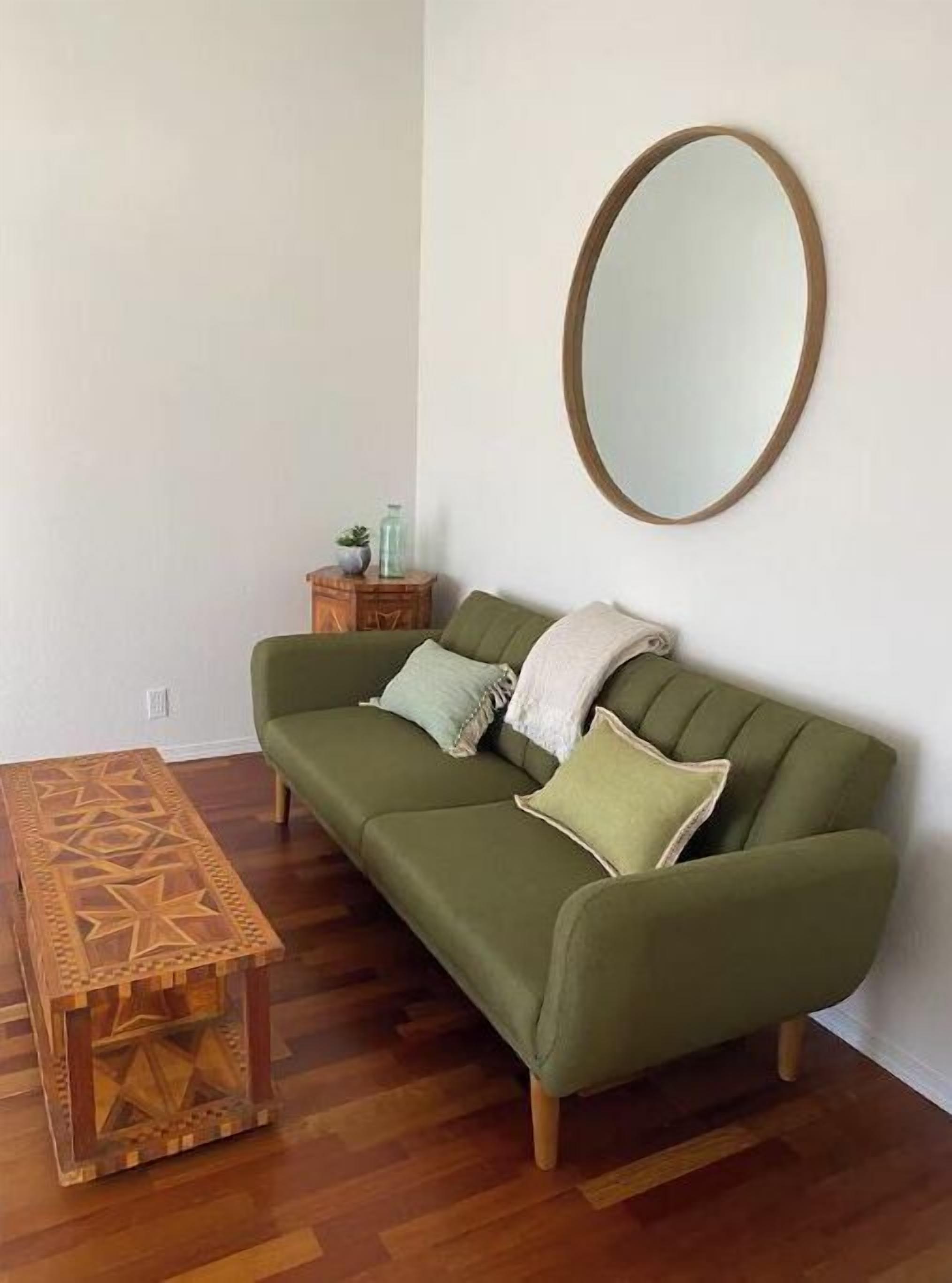 A green sofa with a wooden side table and a mirror on the wall.