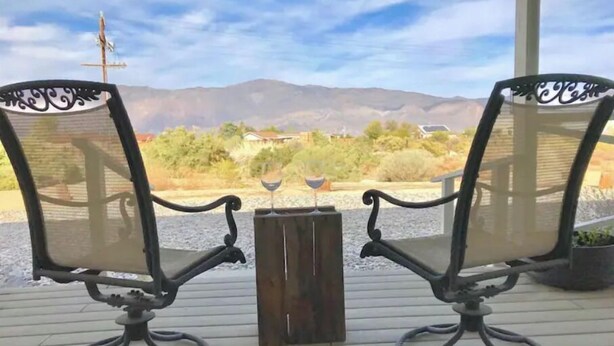 Deux chaises dotées d’une structure en métal et d’un dossier en treillis, placées sur une terrasse en bois, avec vue sur des montagnes et une végétation clairsemée en arrière-plan.