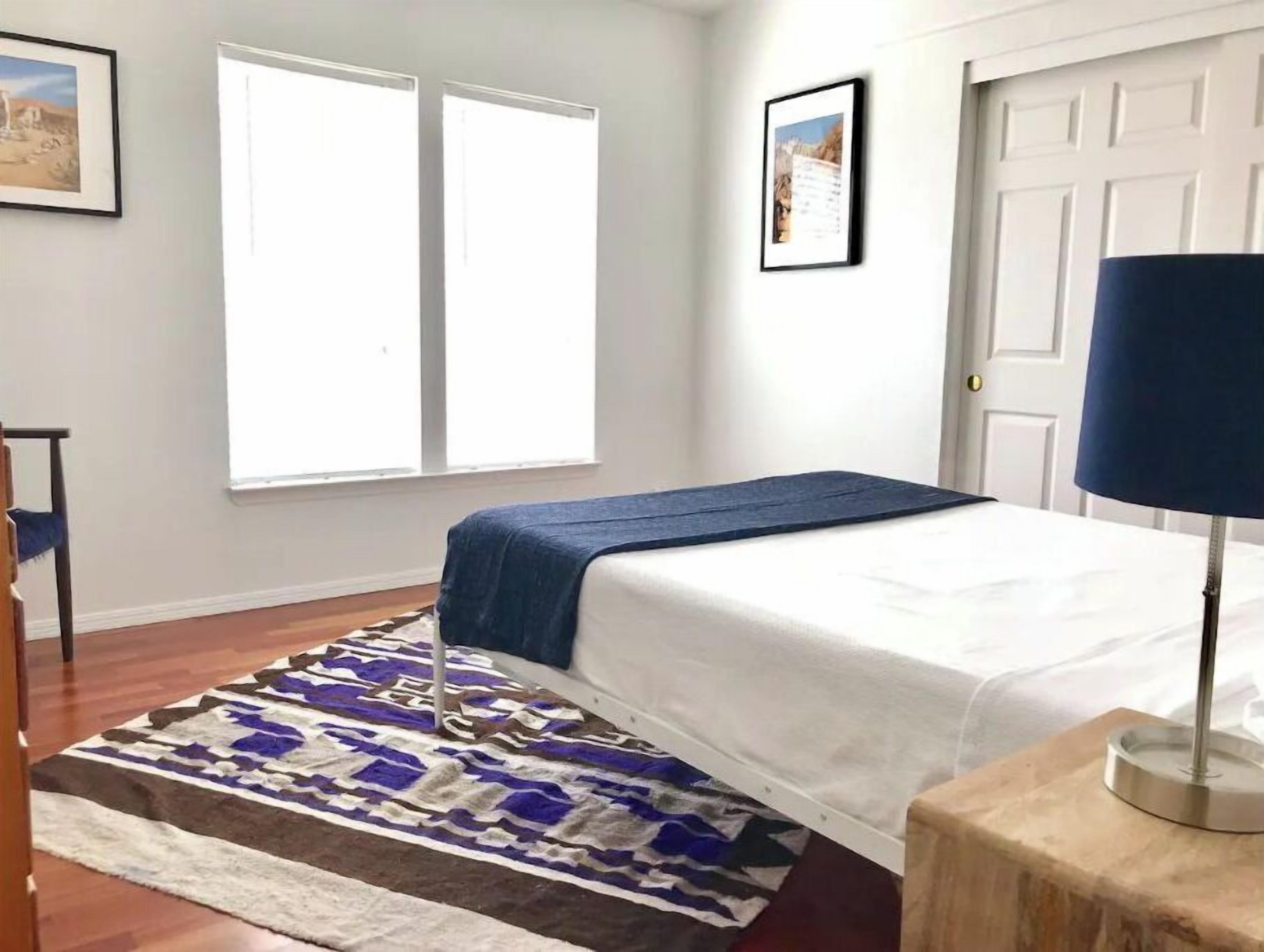 A bedroom with a bed, a window, a door, and a rug.