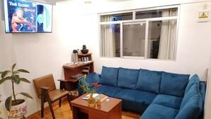 A living room with a blue sofa, wooden coffee table, and a TV mounted on the wall. - El Ave Azul Boutique Hotel Cusco (Cusco)