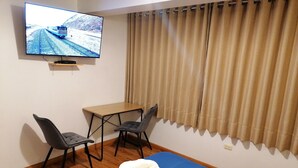 A hotel room with a bed, a desk, two chairs, a television on the wall, and a window with curtains. - El Ave Azul Boutique Hotel Cusco (Cusco)