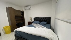 Une chambre à coucher comprenant un lit, une table de chevet, une lampe, une armoire et une poubelle.