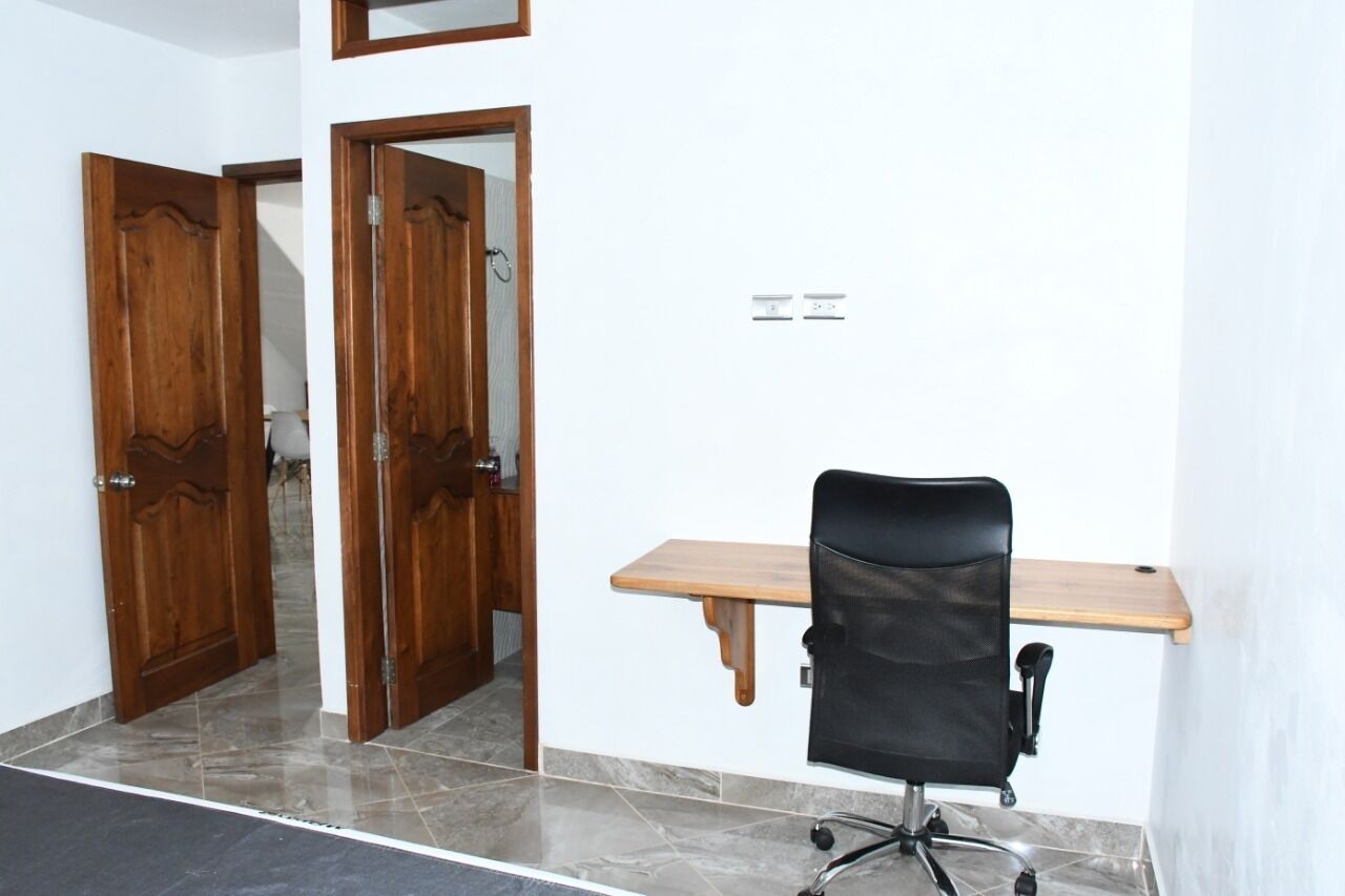 Une pièce avec un bureau en bois, un fauteuil de bureau noir et deux portes en bois.