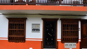 Um edifício com fachada branca e laranja, apresentando uma porta preta com detalhes decorativos e uma pequena caixa elétrica na parede.