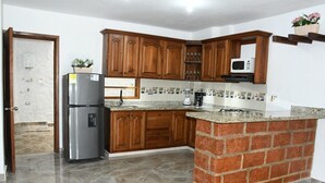 Uma cozinha com armários de madeira, bancada de granito, geladeira, micro-ondas e uma ilha de tijolos.