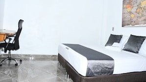 Quarto de hotel com cama, escrivaninha, cadeira e mapa na parede.