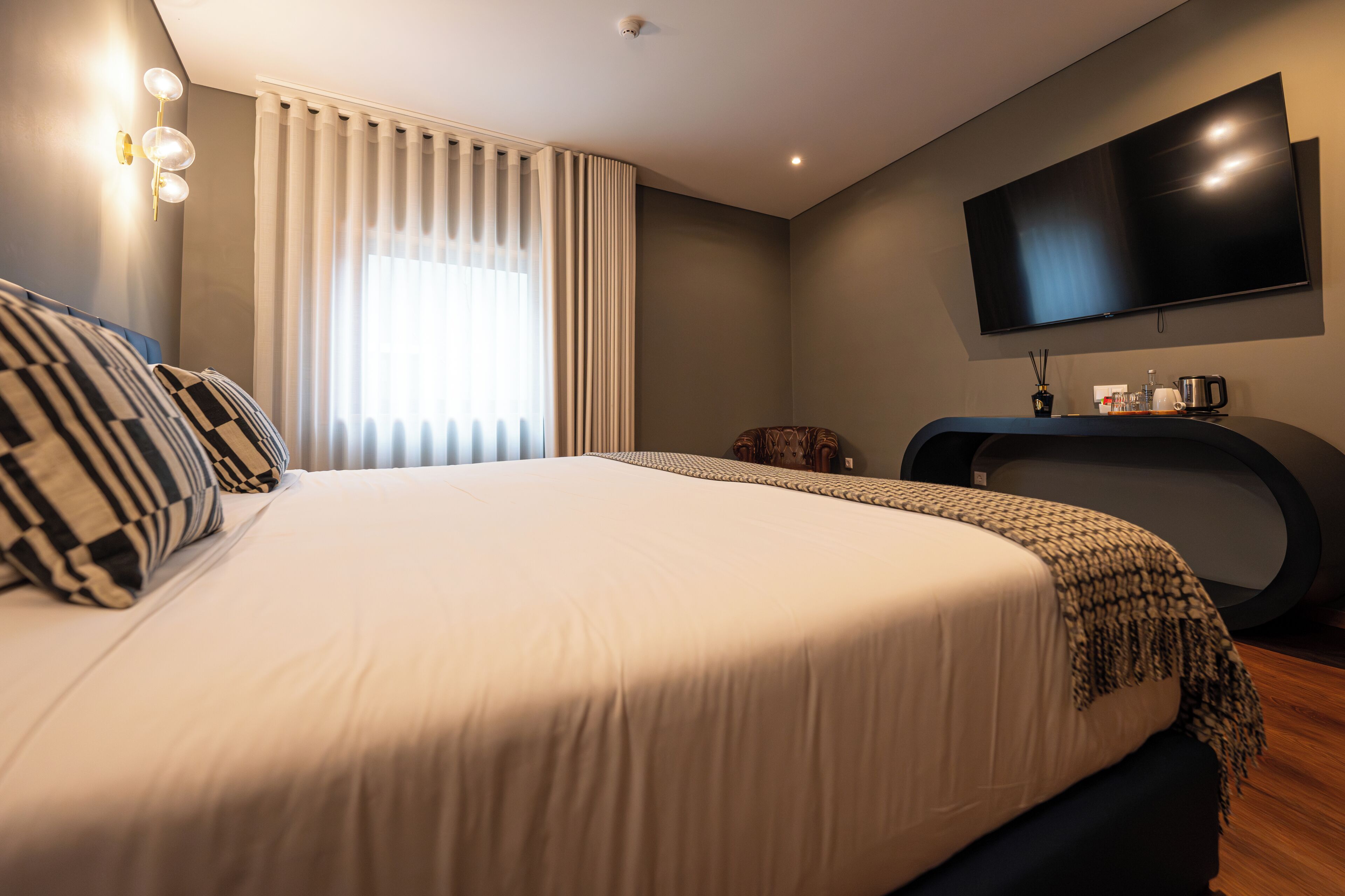 Camera d'albergo moderna con un letto grande, una televisione a schermo piatto, una scrivania con una sedia e una finestra con tende.