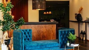 A modern lobby with a blue sofa, a wooden reception desk, and a hanging light fixture. - Santo Thyrso Hotel (Santo Tirso)