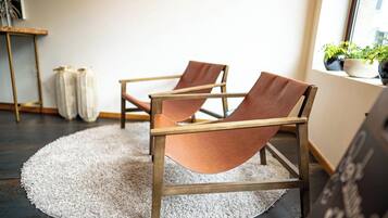 Two leather armchairs with wooden frames on a round rug, a small table with a vase, and potted plants by a window.