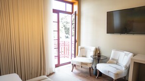 A hotel room with a bed, two white armchairs, a small table with a vase, a flat-screen TV mounted on the wall, and a sliding glass door leading to an outdoor balcony. - Santo Thyrso Hotel (Santo Tirso)
