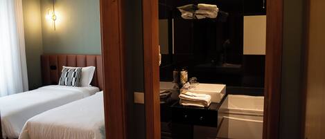 Een hotelkamer met twee bedden, een badkamer met een badkuip en een houten deuropening.