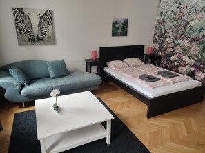 A bedroom with a bed, a sofa, a small table, and a nightstand.