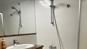 A bathroom with a washing machine, a sink, a shower, and a bathtub.