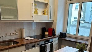 Eine moderne Küche mit weißen Schränken, einer Granit-Arbeitsplatte, einem eingebauten Backofen und einem Fenster mit Blick auf die Straße.