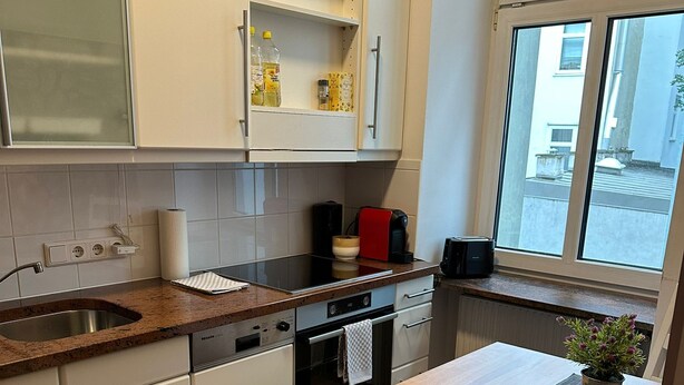 A modern kitchen with white cabinets, a granite countertop, a built-in oven, and a window with a view of the street.