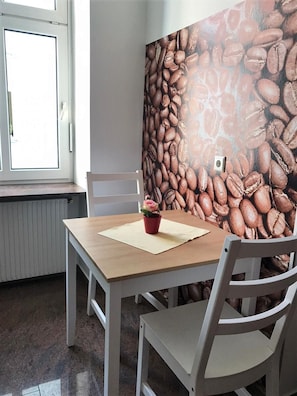 Une pièce avec une table en bois et des chaises blanches, un radiateur et une fenêtre donnant sur l’extérieur.