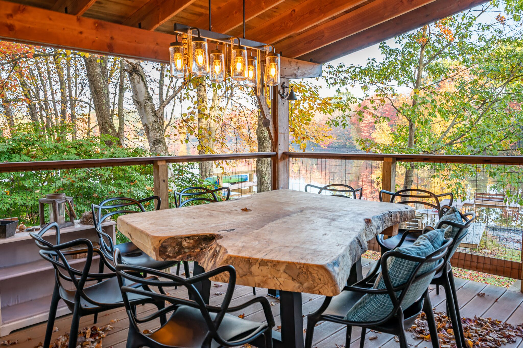 Une terrasse extérieure dotée d’une grande table et de chaises, entourée d’une plateforme en bois et offrant une vue sur les arbres et une clôture.
