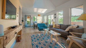 A spacious living room with a fireplace, a blue armchair, a sofa, and a dining area with a table and chairs.