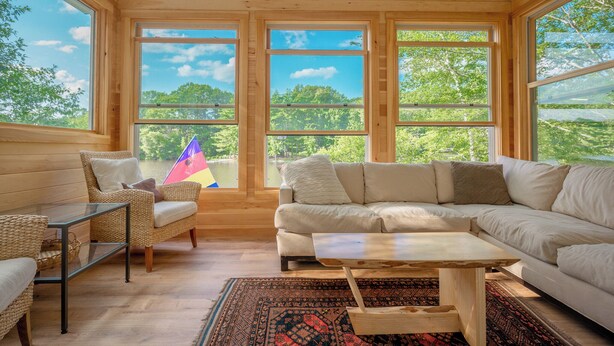 A cozy room with a large window, a sofa, a coffee table, and a wicker chair.