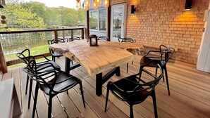 A wooden deck with a large table and chairs, a brick wall, and hanging lights.
