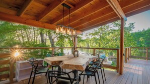 A wooden deck with a table and chairs, overlooking a lake surrounded by trees.