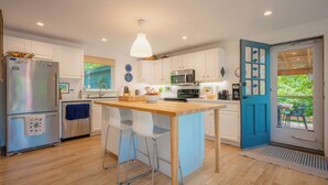 A modern kitchen with white cabinets, a wooden island, and a blue door leading to an outdoor area.